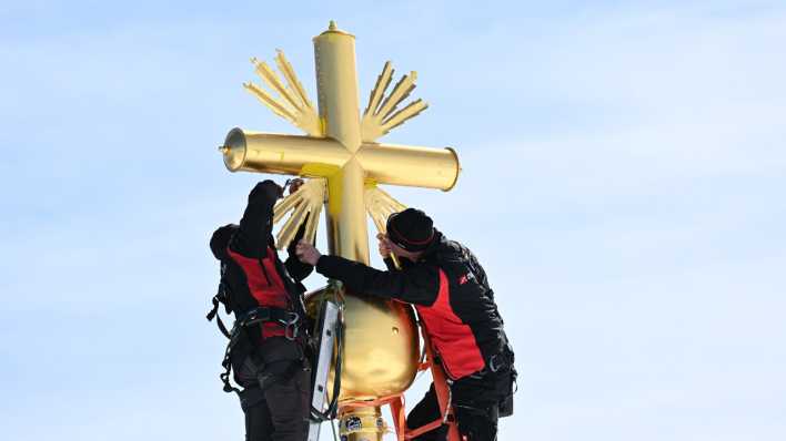Die im Tal restaurierten Strahlen des Gipfelkreuzes der Zugspitze werden von Mitarbeitern wieder am Gipfelkreuz angebracht.