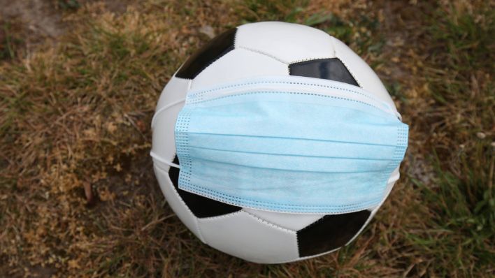 Ein Mundschutzmaske ist über einem Fußball gestülpt (Foto: Imago / Christian Schrödter)