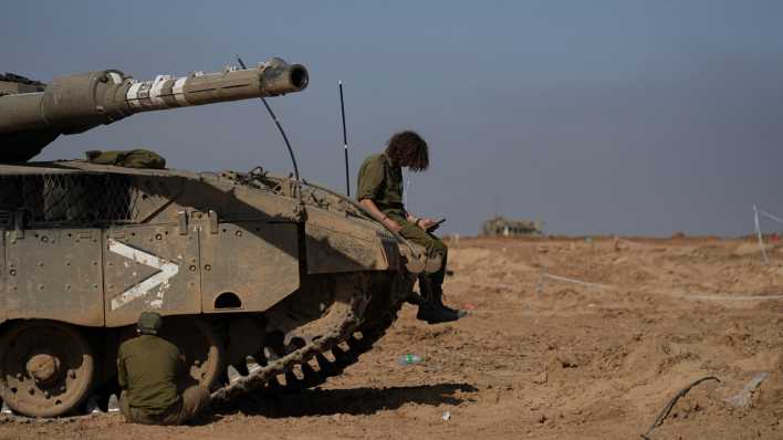 Ein israelischer Soldat sitzt auf einem Panzer und schaut auf ein Smartphone - nach Inkrafttreten einer vorübergehend (Bild: Tsafrir Abayov/AP/dpa)en Feuerpause zwischen Israel und der islamistischen Hamas