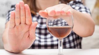 Eine junge Frau hält eine Hand auf ein Weinglas und macht mit der anderen Hand eine ablehnende Geste.