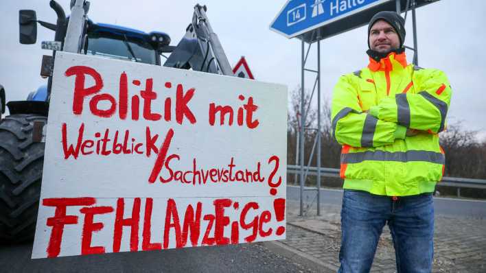 Ein Landwirt steht bei einer Blockade von Bauern der Autobahnauffahrt Leipzig Ost an der A14 neben einem Schild mit der Aufschrift "Politik mit Weitblick/Sachverstand? Fehlanzeige!"