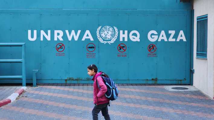 Ein Mädchen geht an der Aufschrift "UNRWA HQ Gaza" in Gaza City vorbei (Bild: picture alliance/ZUMAPRESS/Ashraf Amra)