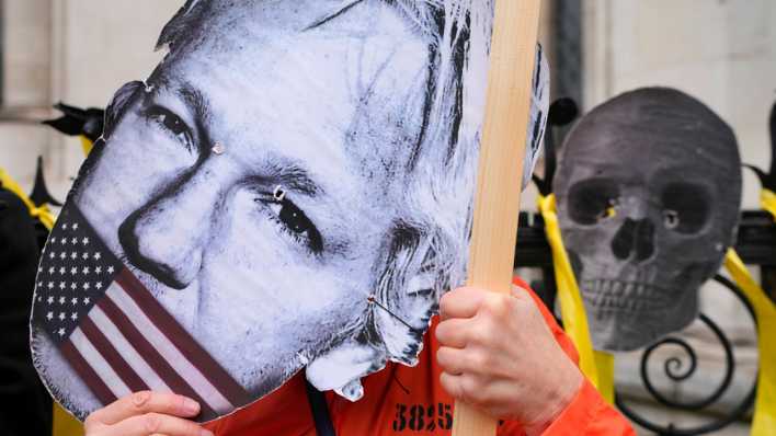 Demonstranten halten eine Maske mit dem Gesicht von Julian Assange