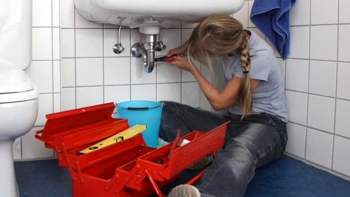 Frau repariert eine defekte Wasserarmatur in einem Badezimmer