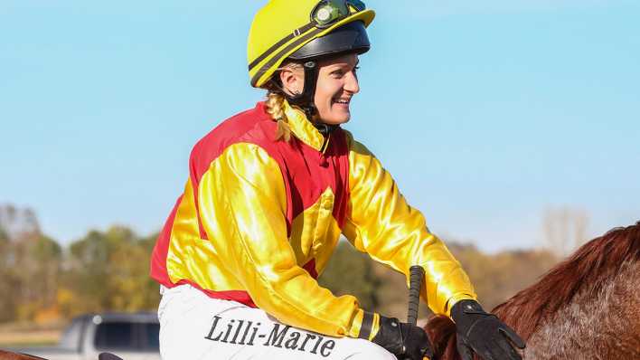 Jockey Lilli Marie Engels sitzt lachend auf dem Rücken eines Pferdes.