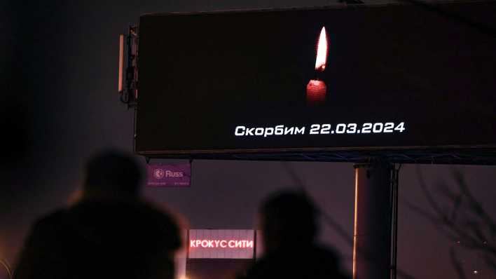 In Moskau laufen Menschen an einer Anzeigetafel vorbei, auf der eine Kerze für die Opfer des 22.03.2024 leuchtet.