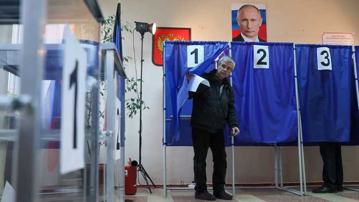 Ein Mann kommt aus einer Wahlkabine. Über den Kabinen hängt ein Porträt von Wladimir Putin.