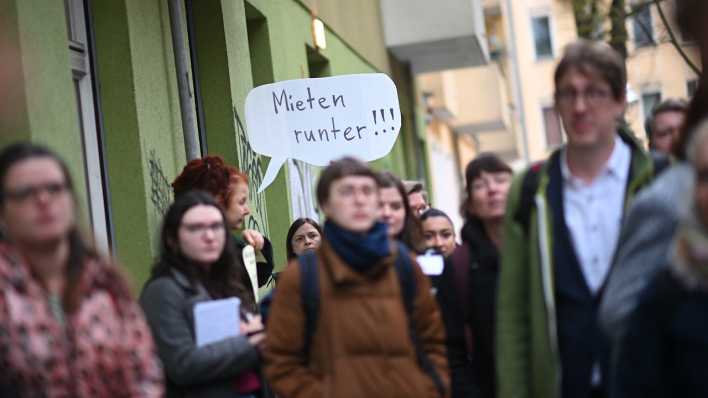 Demonstranten halten bei der Bezirkstour des Berliner Senats mit Journalisten durch Neukölln vor der Tee und Wärmestube Neukölln in der Weisestraße ein Transparent mit der Aufschrift "Mieten runter!!!" hoch.