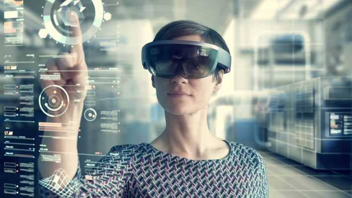 Eine Frau trägt eine Mixed-Reality-Brille und bedient einen transparenten Bildschirm (Bild: imago/Rainer Berg)