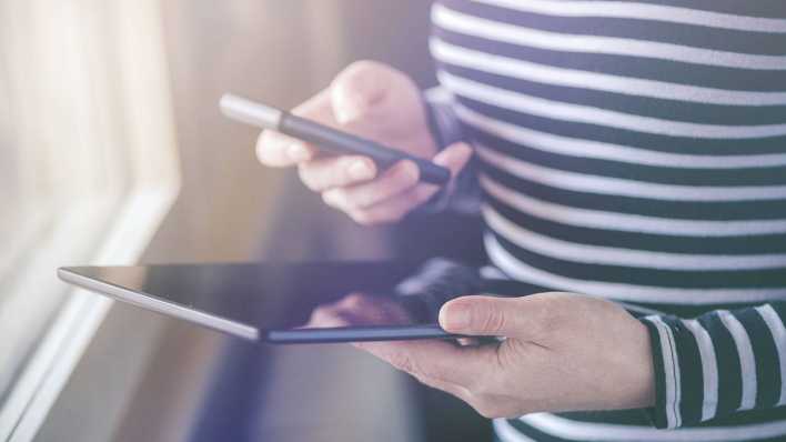 Ein Mensch hält ein Smartphone in der einen, ein Tablet in der anderen Hand Ein Mensch hält ein Smartphone in der einen, ein Tablet in der anderen Hand