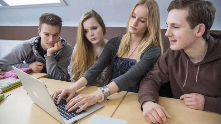 Schüler der Oberstufe eines Gymnasiums um ein Notebook