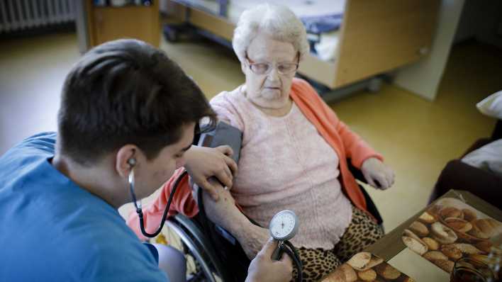 Eine männliche Pflegekraft misst den Blutdruck bei einer älteren Frau im Rollstuhl