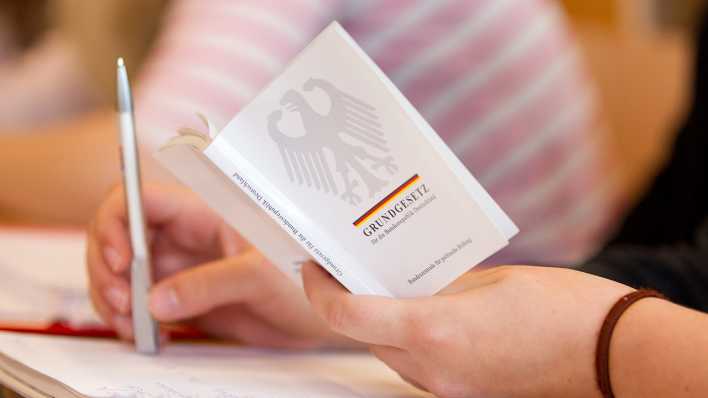 Eine Jura-Studentin hält in einer Vorlesung an der Universität eine Ausgabe vom Grundgesetz in der Hand. (Bild: dpa)