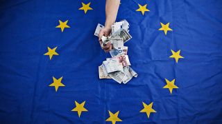 Eine Hand nimmt sich Euro-Scheine, die auf einer Flagge der Europäischen Union liegen. (Bild: imago images/CTK Photo)