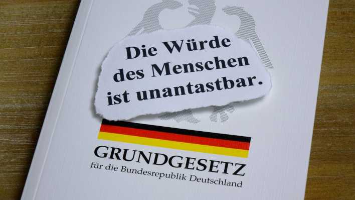 Auf einem Grundgesetz liegen die Worte "Die Würde des Menschen ist unantastbar"