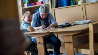 Symboldbild Inklusion in der Schule: Eine Inklusionshelferin unterstützt einen Jungen mit Down-Syndrom bei seinen Hausaufgaben.