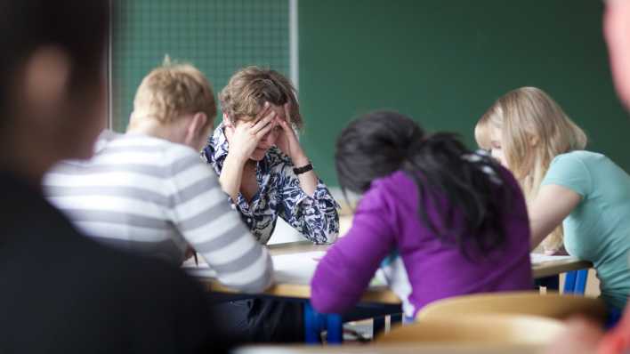 Eine Lehrerin sitzt verzweifelt am Lehrerpult