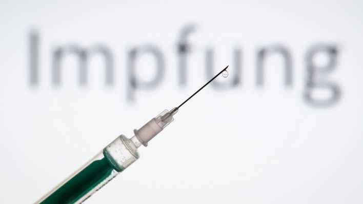 Eine Spritze wird vor den Schriftzug "Impfung" gehalten. (Bild: dpa)