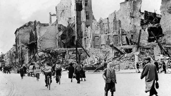 Menschen gehen nach Kriegsende im Mai 1945 auf einer Straße in Berlin an zerstörten Häusern entlang