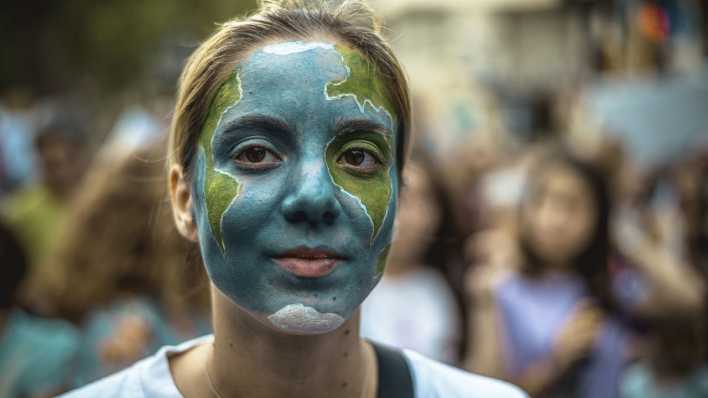Eine Klimaaktivistin hat sich bei einer Demonstration von Fridays for Future in Bracelona eine Weltkarte ins Gesicht gemalt