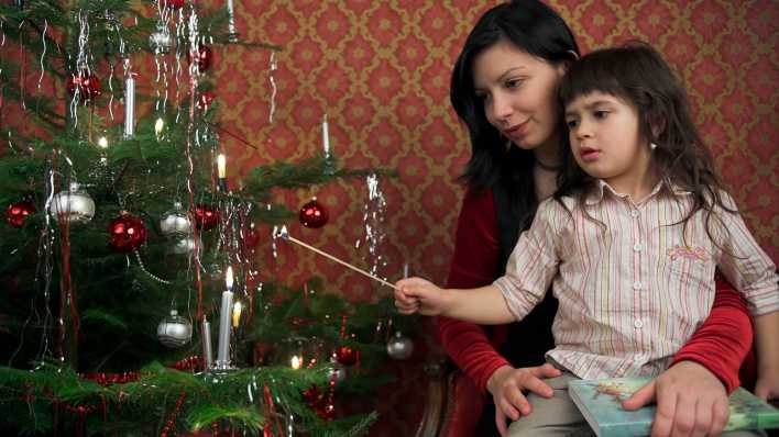 Alleinerziehende Mutter mit Tochter beim Weihnachtskerzen anzünden