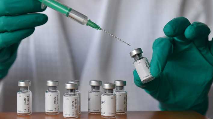 Medizinisches Personal haelt eine Impfspritze und eine Impfdose mit Impfstoff gegen das Coronavirus.