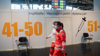 Zwei Mitarbeiterinnen im Corona-Impfzentrum in der Arena in Treptow laufen an den Impfkabinen vorbei. (Bild: picture alliance / dpa)