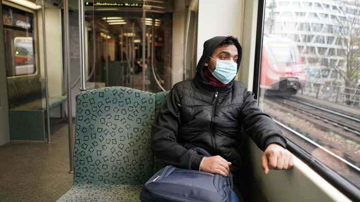 Ein junger Mann mit Mundnasenschutz in einer fast leeren S-Bahn.