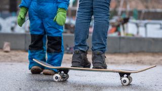 Zwei Kinder stehen bei einem Spielplatz in Berlin. Ein Kind balanciert auf einem Skateboard.