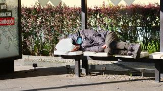 Ein Obdachloser liegt auf Sitzen an einer Bushaltestelle der BVG in und schlaeft. Dabei traegt er eine Maske gegen das Coronavirus.