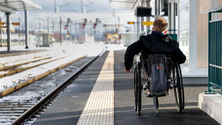 Ein Junge fährt in einem Rollstuhl neben einem Bahngleis.