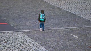 Ein Schüler geht mit seiner Schultasche von der Schule nach Hause.