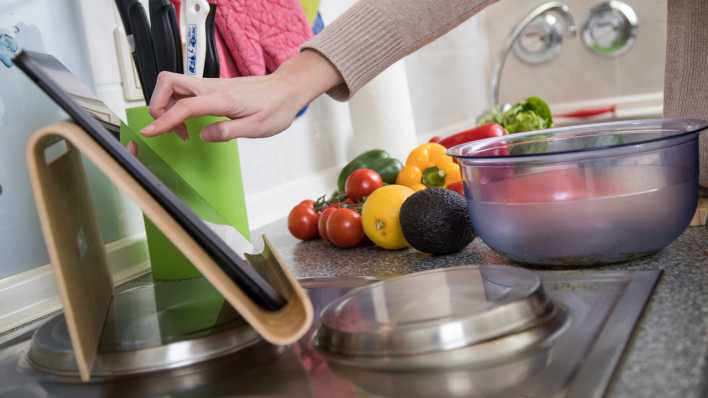 Eine Frau bereitet Essen vor und bedient dabei ein Tablet (Bild: picture alliance/ dpa Themendienst)