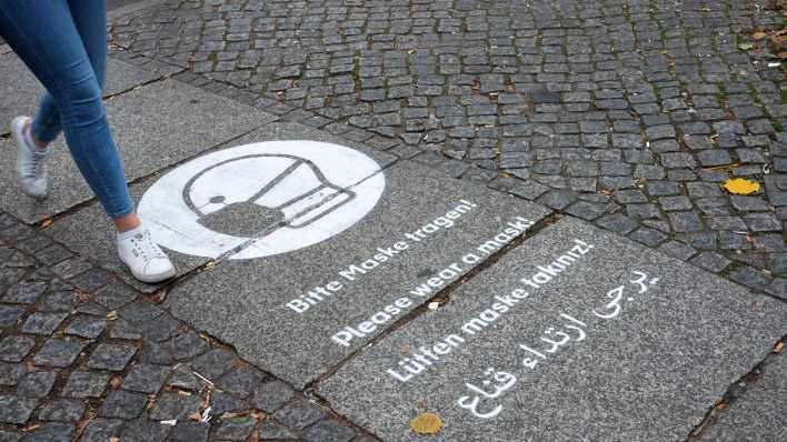 Eine auf dem Pflaster aufgesprühte Erinnerung "Bitte Maske tragen!" steht in mehreren Sprachen auf einem Platz (Bild: picture alliance/ dpa-Zentralbild)