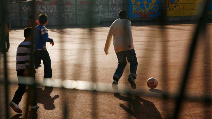 Kinder spielen Ball auf dem Schulhof einer Schule im Bezirk Kreuzberg in Berlin. Mehr als 70 Prozent der Kinder hier haben einen Migrationshintergrund. Die Aufnahme wurde durch einen Zaun fotografiert. Foto: Wolfram Steinberg
