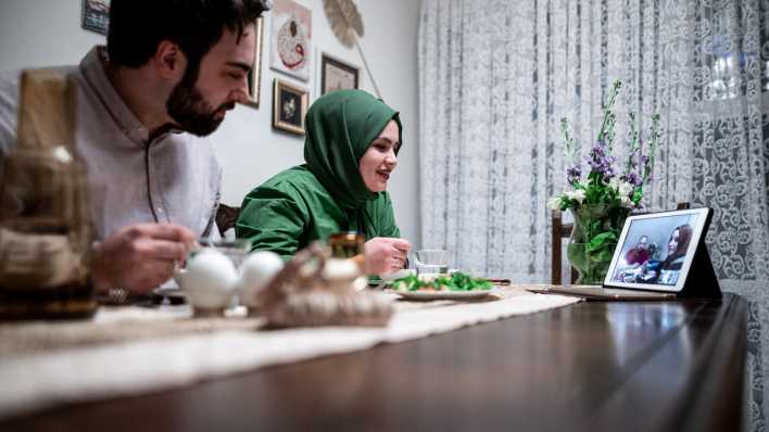 Ein junges Paar sitzt zusammen beim Abendessen und telefoniert mit Freunden. Das Paar ist normalerweise an Ramadan fast täglich bei Freunden oder der Familie eingeladen, durch die Corona-Pandemie verbringen beide das Fastenbrechen zu zweit Zuhause. Gesellschaft gibt es nur mittels Videokonferenz.