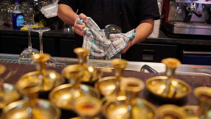 Ein Mitarbeiter eines Restaurants in Berlin poliert die Weingläser.