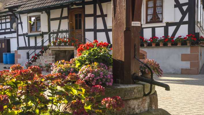 Mit Blumen geschmücktes Fachwerkhaus des Elsass mit altem Brunnen in Hunspach.