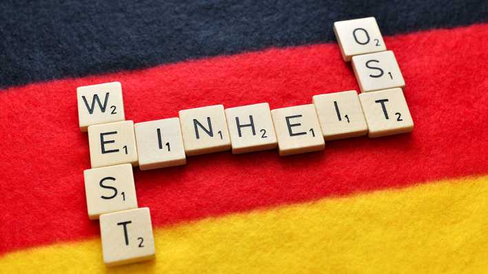 Buchstaben bilden die Schriftzüge Einheit, West und Ost auf einer Deutschlandfahne