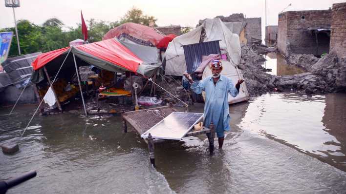 Ein Mann steht in den Fluten in Pakistan vor zerstörten Häusern.