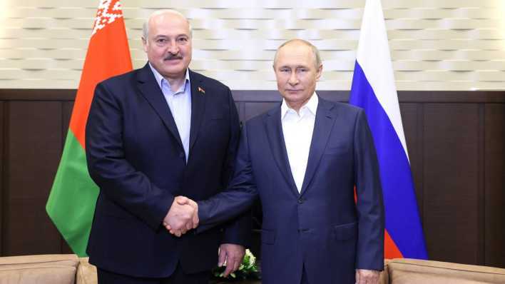 Lukaschenko und Putin schütteln die Hände vor ihren Landesflaggen.