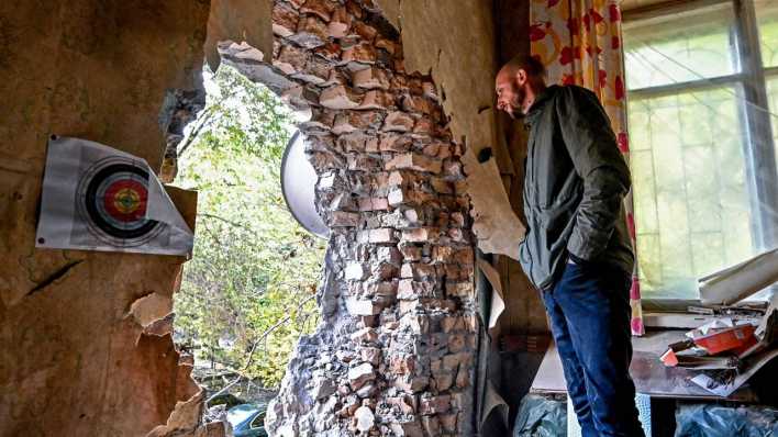 Ein Mann steht in einem zerstörten Haus in der Ukraine.