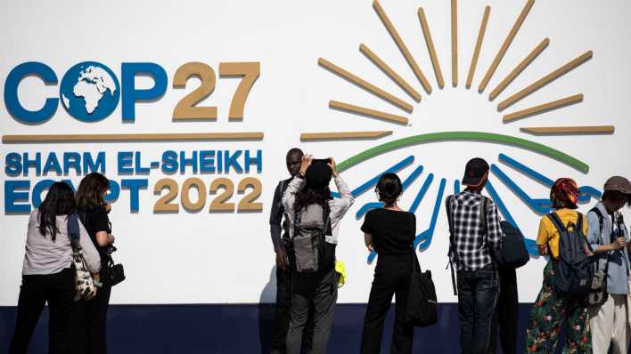 Teilnehmer stehen vor dem Logo des UN-Klimagipfels COP27 im International Convention Center.