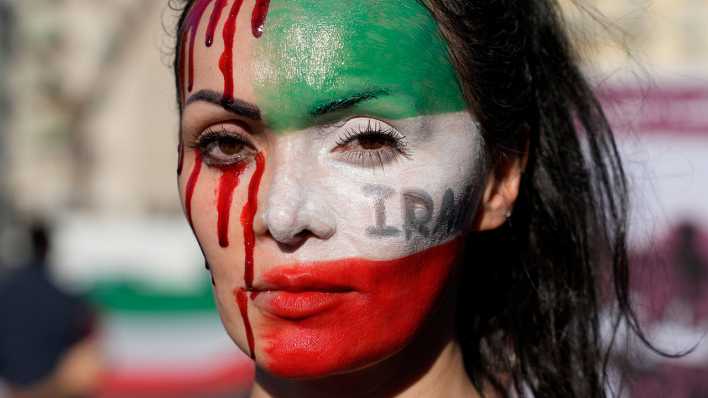 Eine Teilnehmerin einer Solidaritätsdemonstration in Italien mit den Protestierenden im Iran ist mit einer Iranischen Flagge und rotem Blut geschminkt.