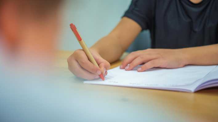 Ein Grundschüler sitzt an einem Tisch und schreibt mit einem Kugelschreiber in sein Heft.