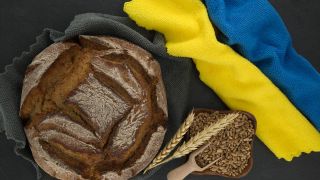 Ein Brotlaib liegt neben zwei Geschirrtüchern, die mit blau und gelb wie die Flagge der Ukraine gelegt sind (Bild: picture alliance / Zoonar)