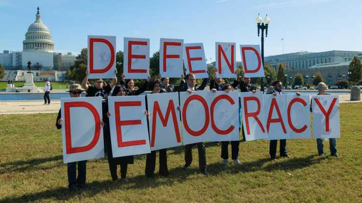 Protestierende halten Buchstaben, die "Defend Democracy" ergeben.