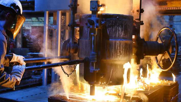 In einem Schmelzbetrieb einer Gießerei füllt ein Gießereimechaniker das bei etwa 1.600 Grad Celsius geschmolzene Metall in bereitgestellte Formen (Bild: picture alliance/dpa)