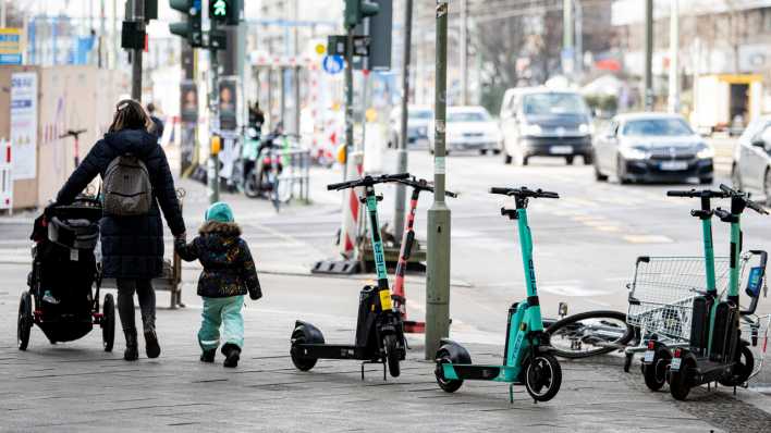 Eine Mutter mit Kind und Kinderwagen läuft an mehrere E-Scootern Berlin-Mitte vorbei.