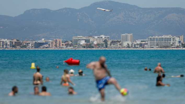 Ein Flugzeug fliegt über das Meer, während Urlauber im Wasser spielen. (Bild: dpa)